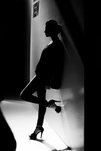 a black and white photograph of a female model resting against a white wall taken in a dark set up with light on the model shot in a studio set up by top creative photographer ashish gurbani based in pune india