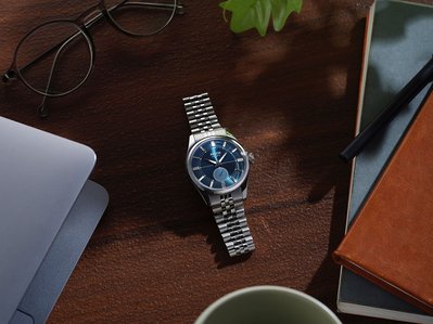 a blue dial luxury watch placed on a laptop study table with a wooden background in a professional product photography studio in Pune