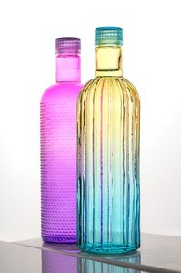 a product photoshoot taken in a studio setting of one pink and one yellow and blue transparent bottle kept on a reflective surface with a white background shot by best product photographer ashish gurbani based in pune india