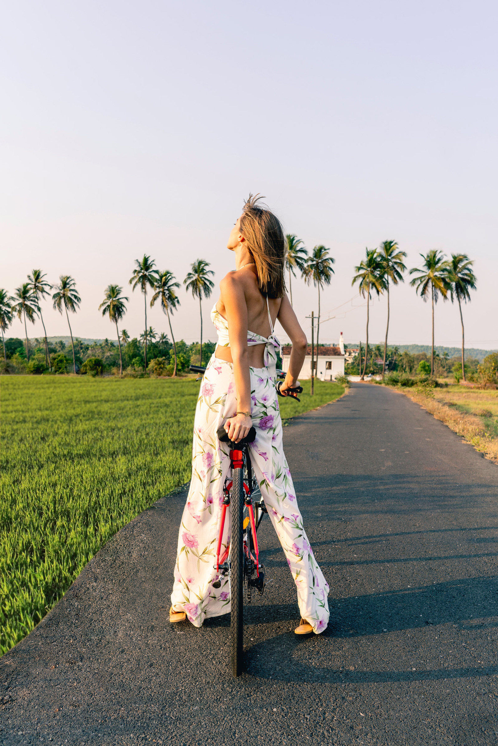 a beautiful female model cycling down the streets of goa between the lush green fields and coconut trees posing for westin goa brand campaign photoshoot for online advertising photographer