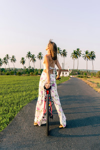 a beautiful female model cycling down the streets of goa between the lush green fields and coconut trees posing for westin goa brand campaign photoshoot for online advertising photographer