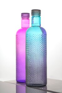 a professional product photoshoot taken in a studio setting of one pink and one blue transparent bottle on a reflective surface with a white background shot by best still life photographer ashish gurbani based in pune india