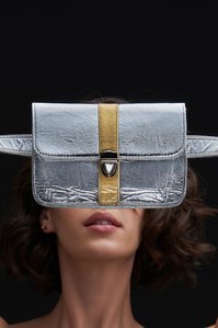 A silver and gold bag is placed in front of a model while the model is out of focus in the bag is in focus