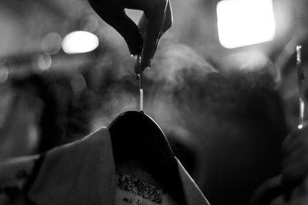 a candid photograph taken in black and white of a female hand holding a collared shirt on a hanger with lights and smoke blurred in the background shot by leading advertising photographer ashish gurbani based in pune india