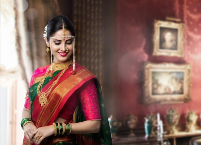 Portrait of a model wearing indian gold jewellery in a red Maharashtrian saree posing in front of a luxurious hall for a jewellery brand photoshoot Pn gadgil in a studio lighting setup shot by leading commercial photographer.