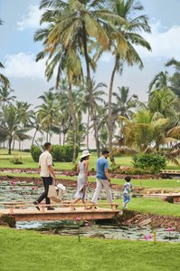 a family walking in a green luscious garden photographed for a leading brand photography with their butler on the way to a picnic in goa india