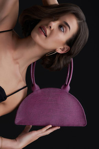 a twisted angle given to a simple photograph of a female model holding a wine red leather bad for a luxury brand shoot in studio lighting setup in mumbai