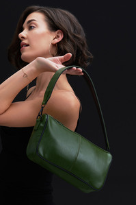 An olive green bag is hanging of a model shoulder wearing a black dress ready to go out for dinner