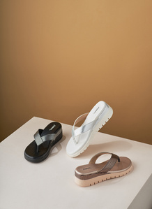a pair of three slippers placed on a white box and brown background with studio lighting for footwear brand photography in india