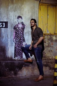 a professional fashion photoshoot of a Male model taken in an outdoor setting posing with graffiti art of a girl standing with flowers in a late night walk with best ad photographer ashish gurbani based in mumbai india