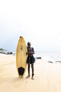 A boy posing with a surfboard on the beach, wearing his swimming trunks shot by Ashish Gurbani top travel photographer based in Mumbai India.