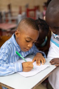 Young boy, assisted by his friend, practicing how to write on a single piece of paper shot by Ashish Gurbani best fashion photographer based in Mumbai India.