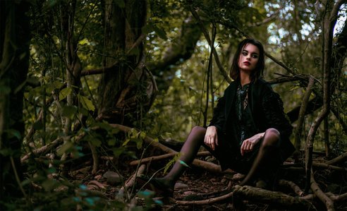 portrait photoshoot of a female model wearing a long sleeve black dress sitting down on branches of a tree in an outdoor setup shot by leading fashion photographer based in pune, india