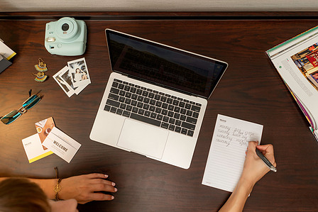 a top down flatlay of a model sitting in her hotel room writing down the journey of her holiday with her laptop on the desk