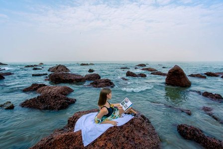 a serene image of a beautiful model laying down on a rock reading a book while hearing the sound of the waves on a goa beach in India photographed by a leading advertising photographer for hospitality based in mumbai india