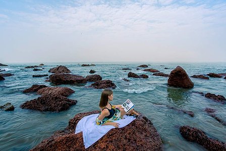 a serene image of a beautiful model laying down on a rock reading a book while hearing the sound of the waves on a goa beach in India photographed by a leading advertising photographer for hospitality based in mumbai india