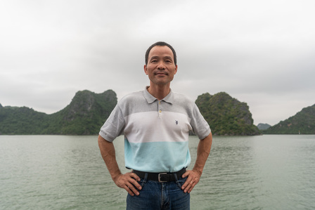 a landscape photograph of a Vietnamese man standing in front of a river and hills under a cloudy sky professionally shot by best landscape photographer ashish gurbani based in pune india