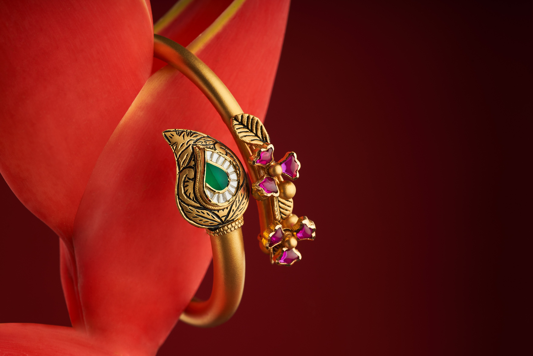 a professional product photoshoot of a golden bangle with green emerald and pink rare stones on a rare flower shot by leading product photographer ashish gurbani specialising in jewellery imagery based in pune india