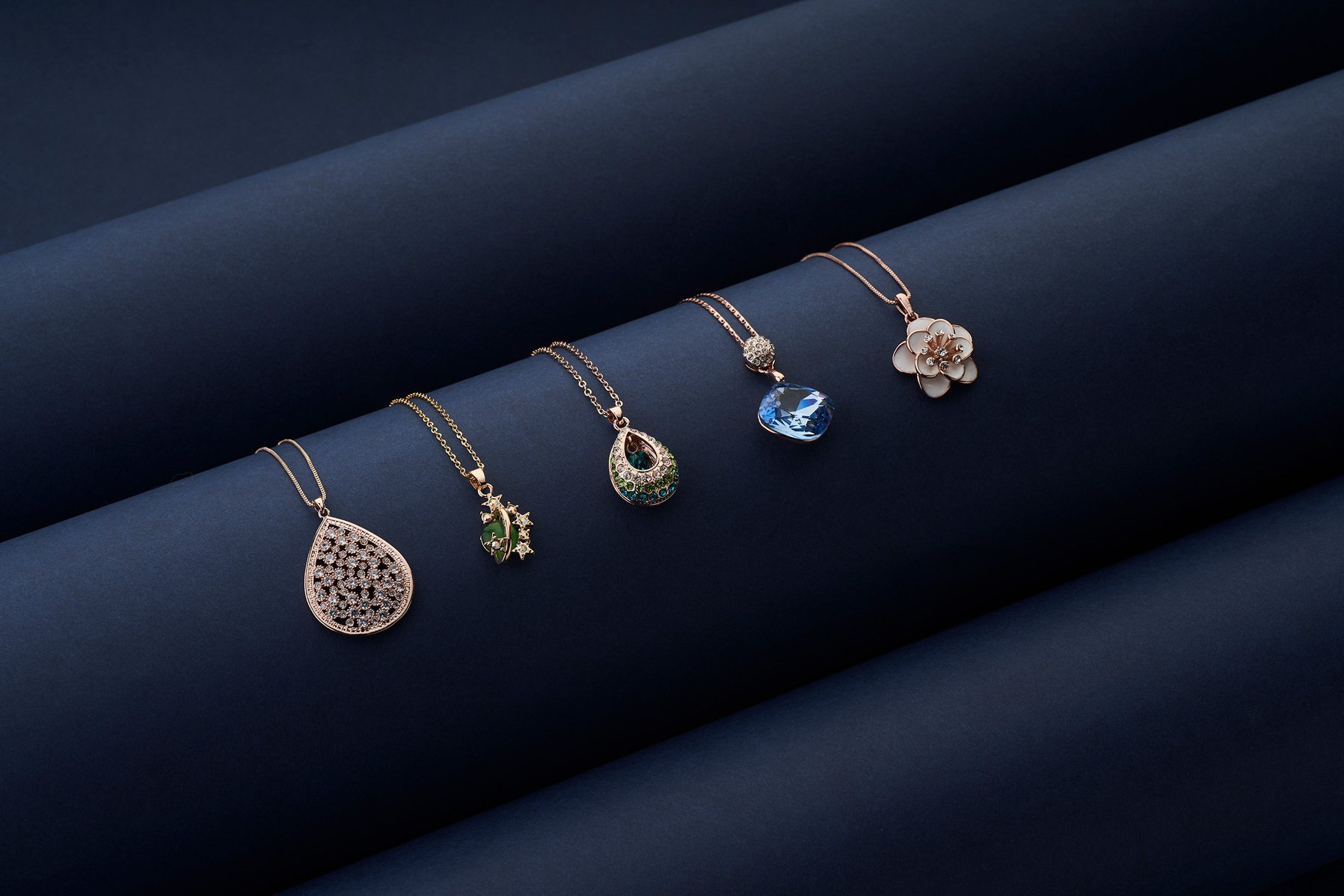 a jewellery product shoot of multiple pendants in a rose gold necklaces shot in studio light on blue background using minimalism approach photography by best jewellery photographer for eCommerce brands based in pune india