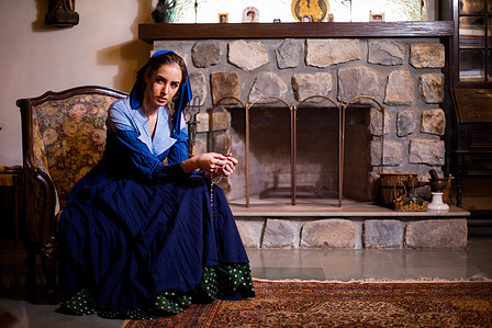 a girl dressed in antique farm girl styling costumes sitting by a rock fireplace in an old rustic house shot by best lifestyle photographer based in mumbai india