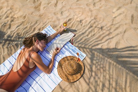 a beautiful indian girl model laying down on the beach sand writing stories on her book in the tree shadow shot by best advertising photographer for an advertising campaign for westin goa based in india