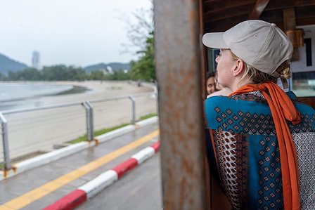 professional candid photograph of a female looking out of a window at a road and sidewalk with a beach and hills blurred out in the background shot by best landscape photographer ashish gurbani based in pune india