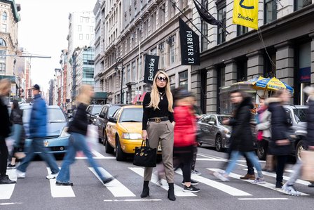 professional photograph of a female model standing in the middle of a busy road on a zebra crossing with traffic and a blurred out rush of people walking behind her shot by leading fashion photographer based in pune india 