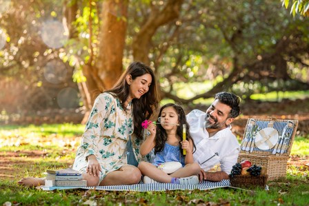 family of father mother and daughter out in the garden for a picnic with a picnic basket and books playing with bubbles photoshoot for a lifestyle advertising campaign shoot by leading advertising photographer based in Mumbai