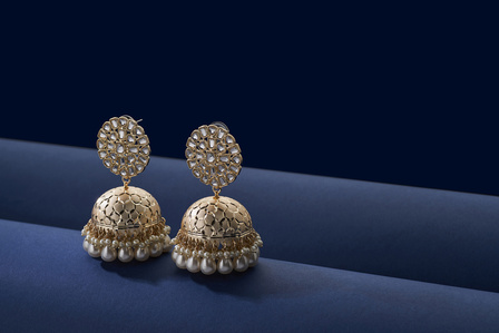 a pair of diamond and gold jhumkas placed on a blue set for brand photoshoot jewellery photo in mumbai
 