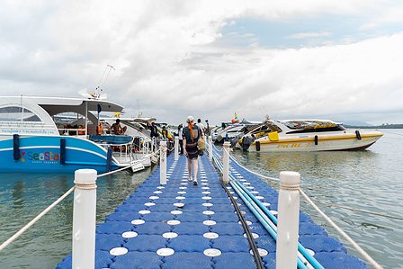 a candid landscape photograph professionally shot of people walking on a blue path on top of water with boats on both sides and a cloudy blue sky taken by top landscape photographer ashish gurbani based in pune india