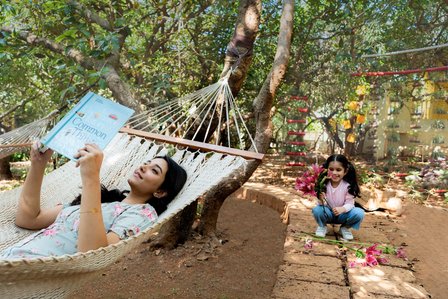 lady swinging on a hammock while reading a book while her daughter plays with flowers in the garden for campaign shoot of hotel brand by best advertising photographer based in Mumbai India