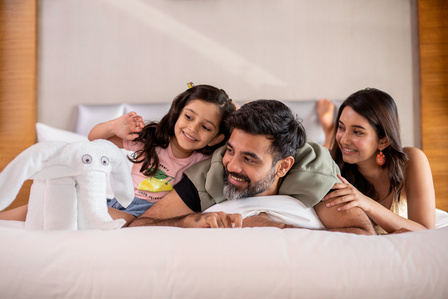 Parents lying down in hotel room on the bed playing with their daughter and showing towel art elephant advertising photoshoot for leading hotel brand Marriott India  by top lifestyle photographer based in Mumbai and Pune India.
