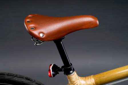 A product photograph of a seat with a brown leather cover of a yellow cycle with red light and tyre in frame shot with a grey background in studio setup by leading product photographer Ashish Gurbani based in Pune, India