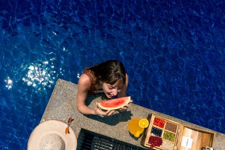 a gorgeous girl enjoying a warm summer afternoon in a deep blue swimming pool eating watermelon amongst other fruits captured by indias best advertising photographer for brand campaigns based in mumbai india