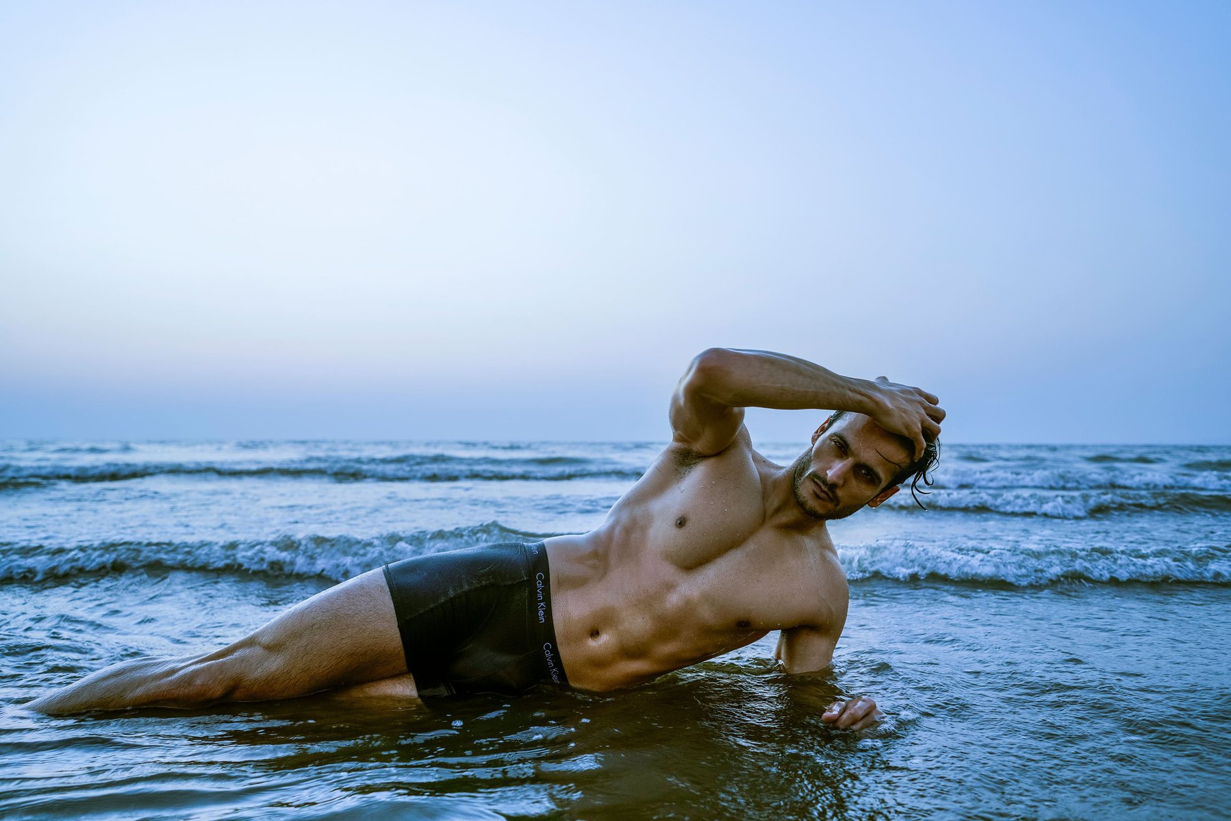 a professional evening sunset photoshoot with leading fashion model and actor angel Singh on a beach lying among the waves shot by best advertising photographer ashish gurbani based in Mumbai india
