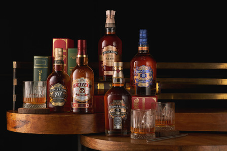 A group of Chivas Regal whiskey bottles styled neatly with books on top of a wooden table was photographed by an e-commerce photographer in Pune, India.

