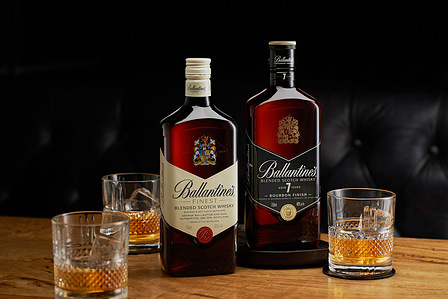 a rustic wooden bar showcasing two ballentines bottles with a collection of whiskey glasses photographed by advertising commercial photographer in india

