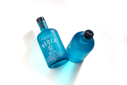 a beautiful emerald blue gin bottles seqer bottled in goa shot in studio lighting setup against a white background by leading alcohol brand photographer based in pune india