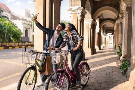 a young cute couple taking a selfie while standing with their cycles in mumbai for a brand campaign photoshoot by best commercial people photographer based in mumbai india