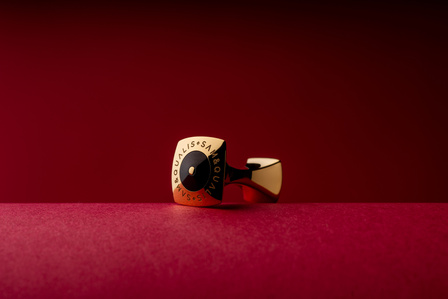 a minimature golden cufflink shot on a red background for marketing puposes by creative product photographer based in pune india 