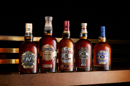 A collection of Chivas Regal whiskey bottles lined up neatly on top of a wooden table photographed by an e-commerce photographer in Pune, India.