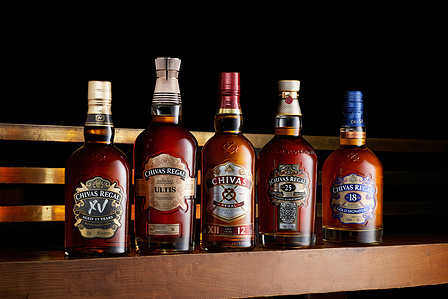 A collection of Chivas Regal whiskey bottles lined up neatly on top of a wooden table photographed by an e-commerce photographer in Pune, India.