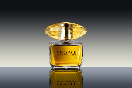 a Versace yellow diamond bottle kept on a black glass setup with edge lighting in background shot by one of the best perfume and cosmetics photographer specilising in luxury products and brands based in pune india