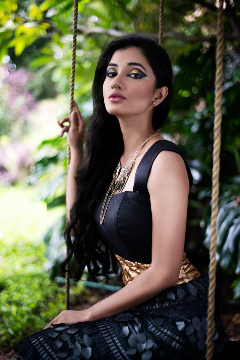 model posing while sitting on swing in black designer gown and green natural background for top fashion photographer based in mumbai india