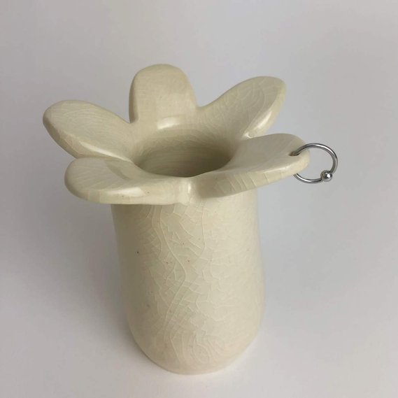  a vase with petals at the top, glazed in an off-white crackled glossy coating. one of the petals is pierced with a silver hoop