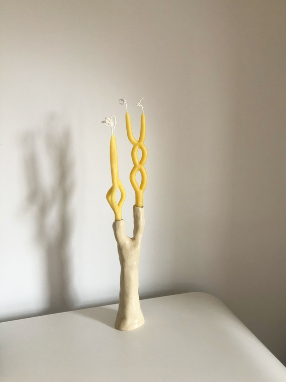 a two-tiered, glossy, off-white candelabra holding avant-garde yellow beeswax candles on a white table