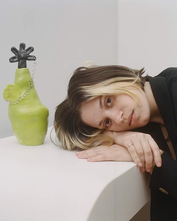 hayley rests her head on a white table next to her green and black floral piece.
