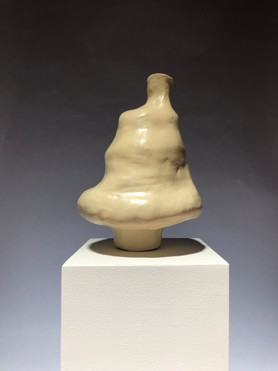 a beige lumpy vase sitting on a white pedestal