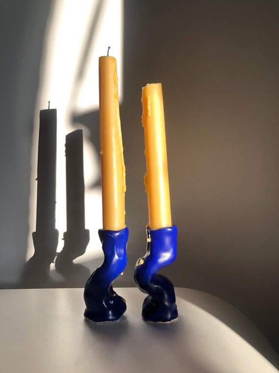 two wavy, lump candlesticks on a white table in a bright blue glaze with two beeswax candles
