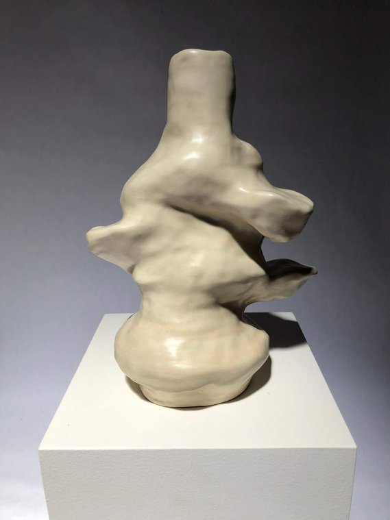 off-white lumpy clustered vessel sits on a white pedestal. reminiscent of mushrooms